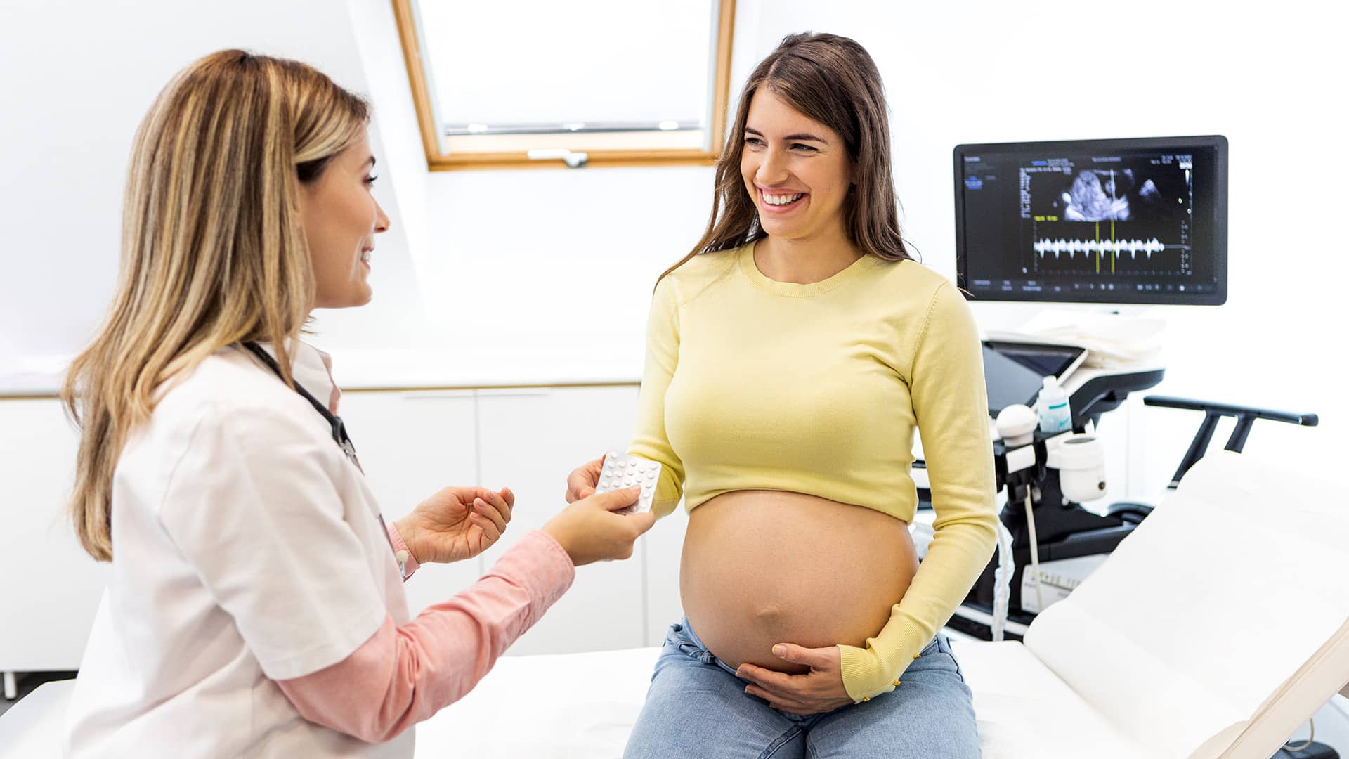 Ärztin gibt einer schwangeren Frau nach dem Ultraschall ein Blister Tabletten
