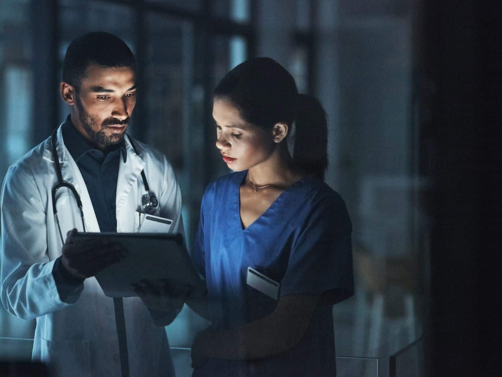Ein Arzt arbeitet am Tablet zusammen mit einer Pflegerin nachts im Krankenhaus