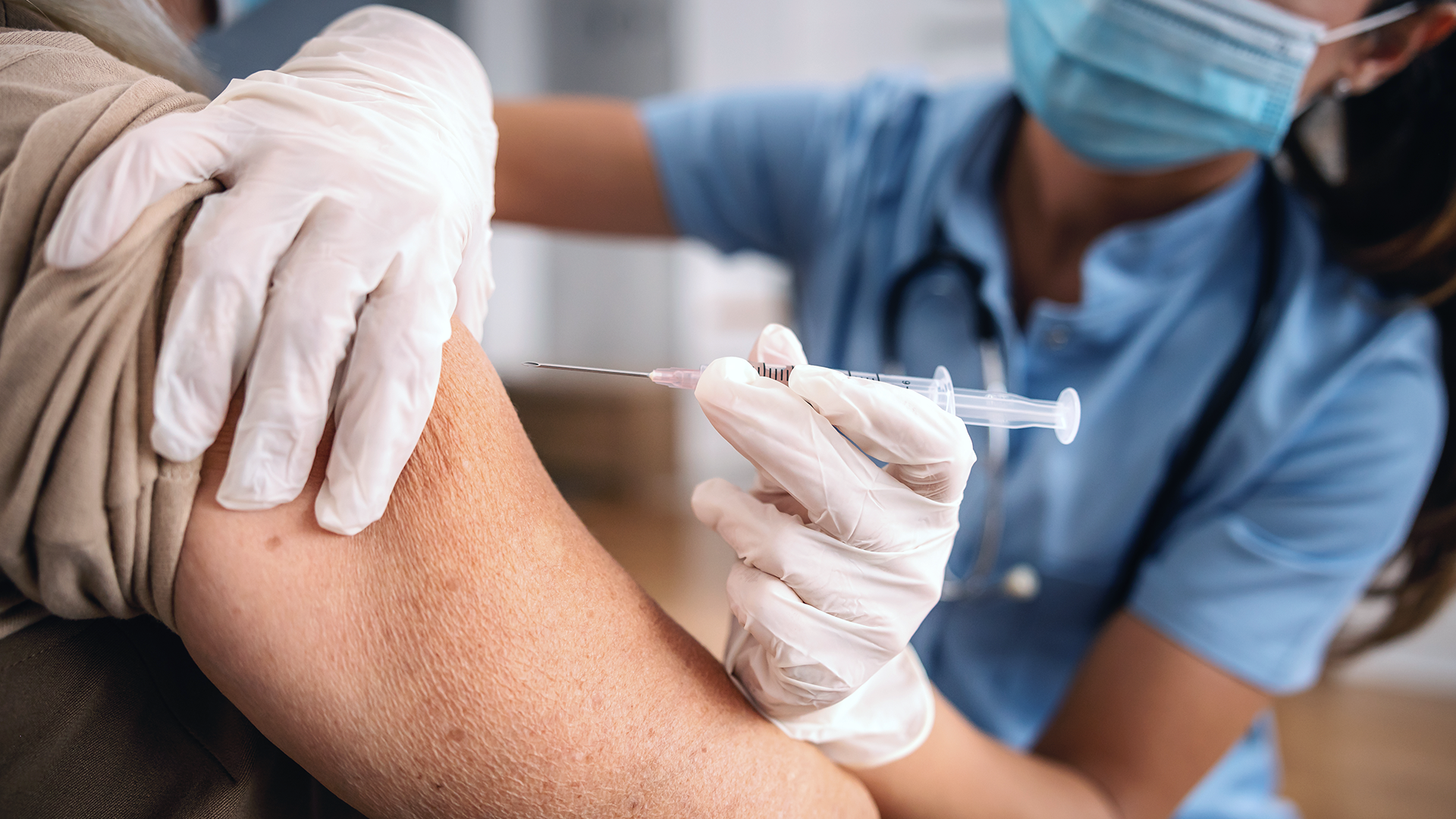 Junge Arzthelferin impft Person mit Spritze zur Vorsorge gegen die Grippe.